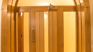 A wooden revolving door with a handle, leading to a room with a tiled floor. - Newcastle Jesmond Hotel (Newcastle-upon-Tyne)