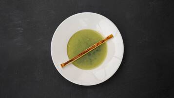 Um prato branco com líquido verde e um pau de canela sobre uma superfície preta.