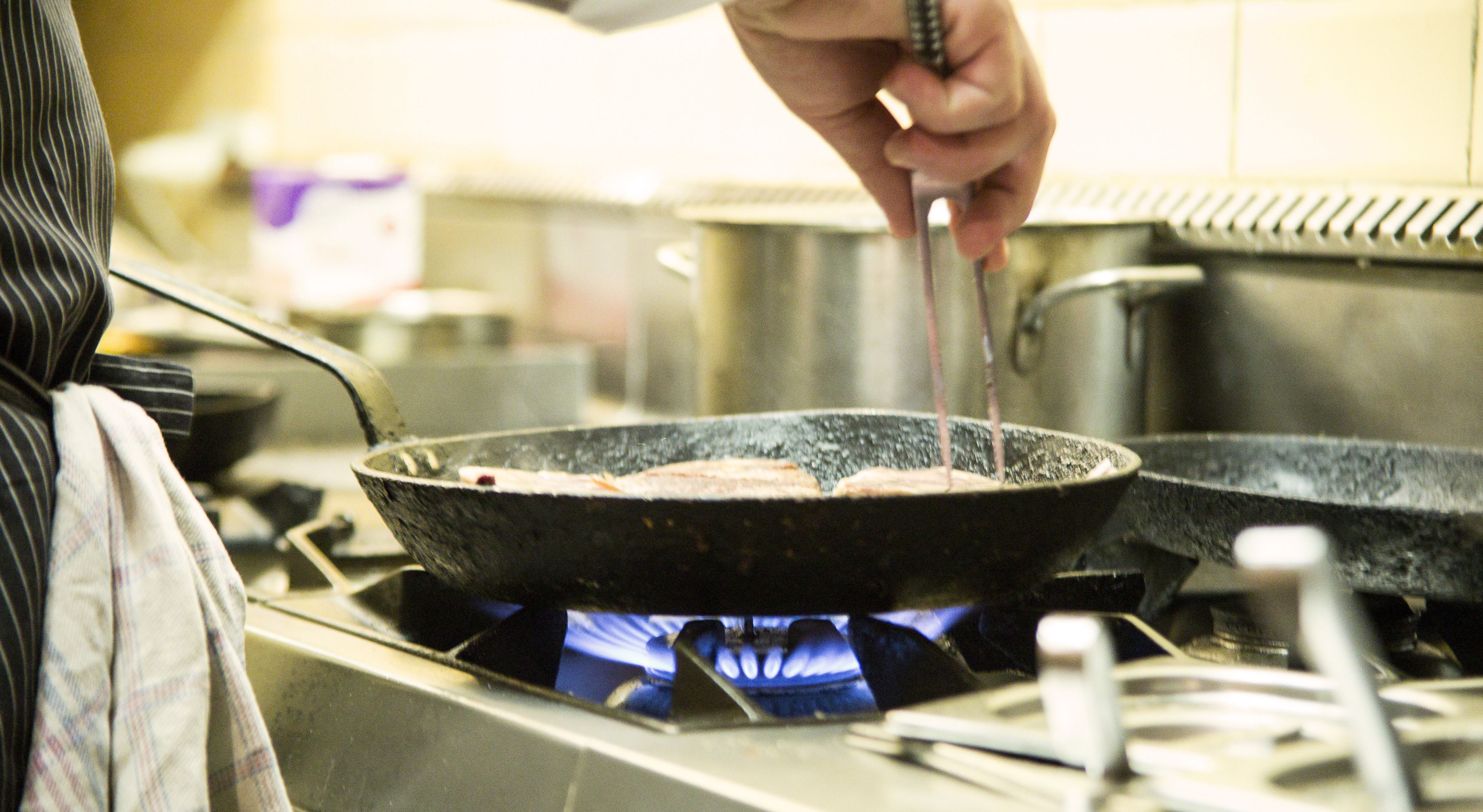 Una persona cucina in una cucina con una padella sul fornello.