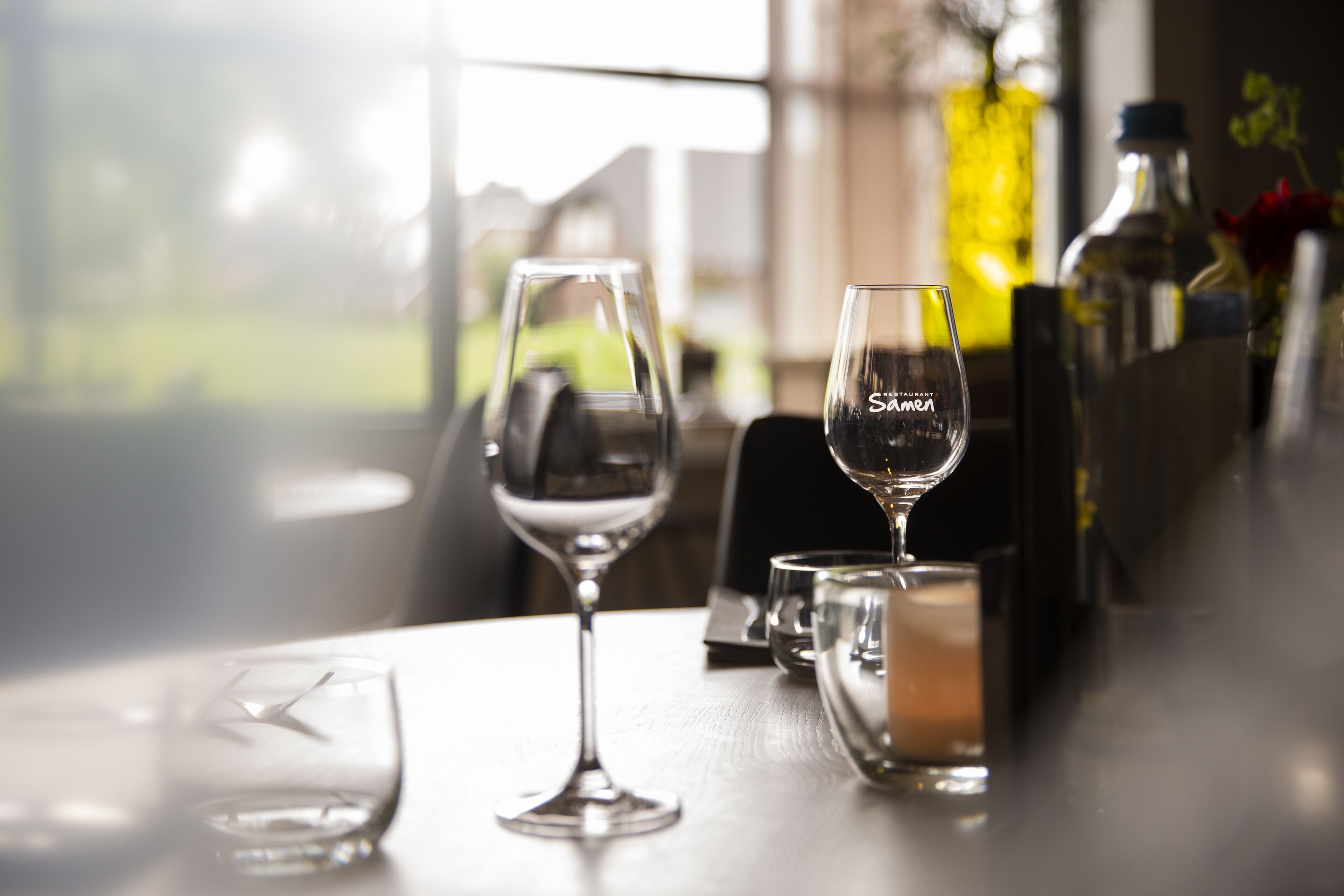Et bord med to vinglas, et glas vin, en flaske olivenolie og en vandflaske.