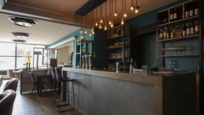Zona de bar moderna con una barra larga, taburetes y estanterías llenas de botellas y vasos.