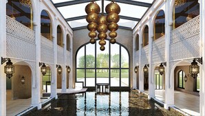 Una piscina interior con techo de cristal, columnas blancas ornamentadas y decoraciones esféricas colgantes.