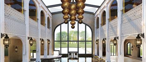 An indoor swimming pool with a glass ceiling, ornate white columns, and hanging spherical decorations.