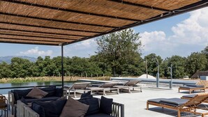 Een buitenruimte met terras, rieten dak, beklede banken en houten tafels.