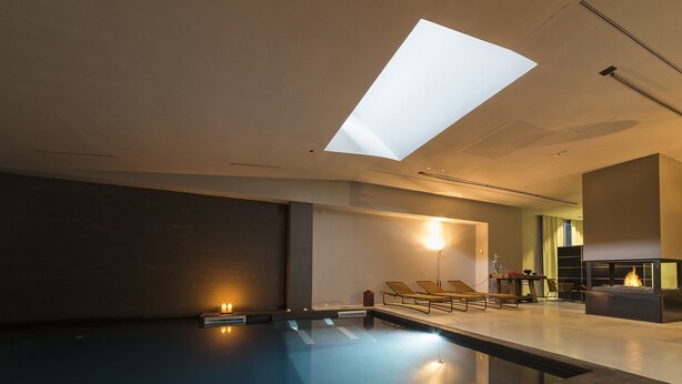 Een modern binnenzwembad met dakraam, lounge fauteuils en een open haard.