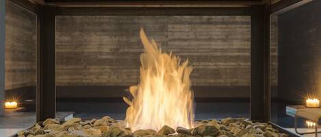 A fire feature with a stone surround, set in a room with a wooden wall and a metal frame.