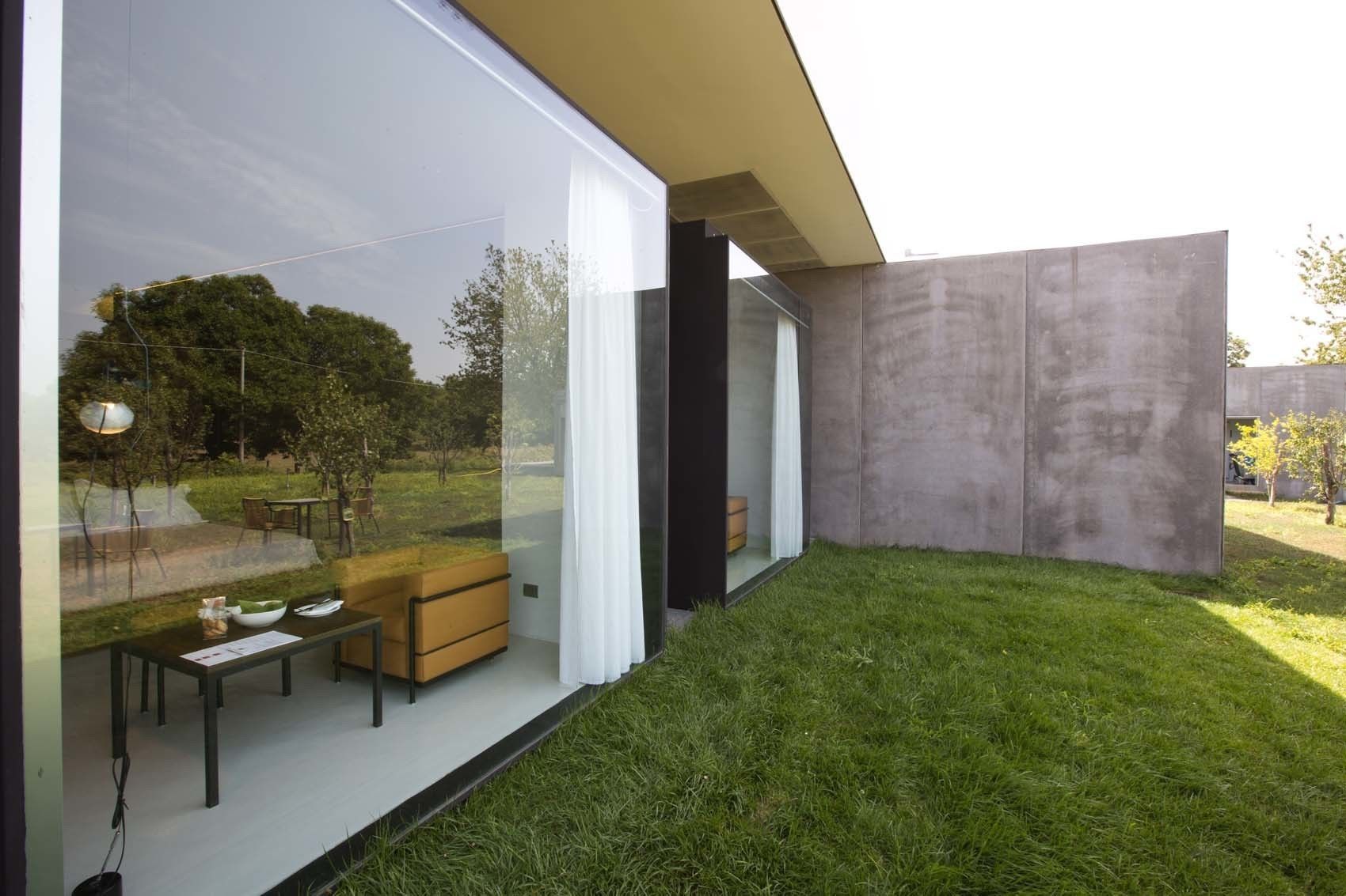 A modern house with a glass wall, a grassy yard, and a concrete structure.