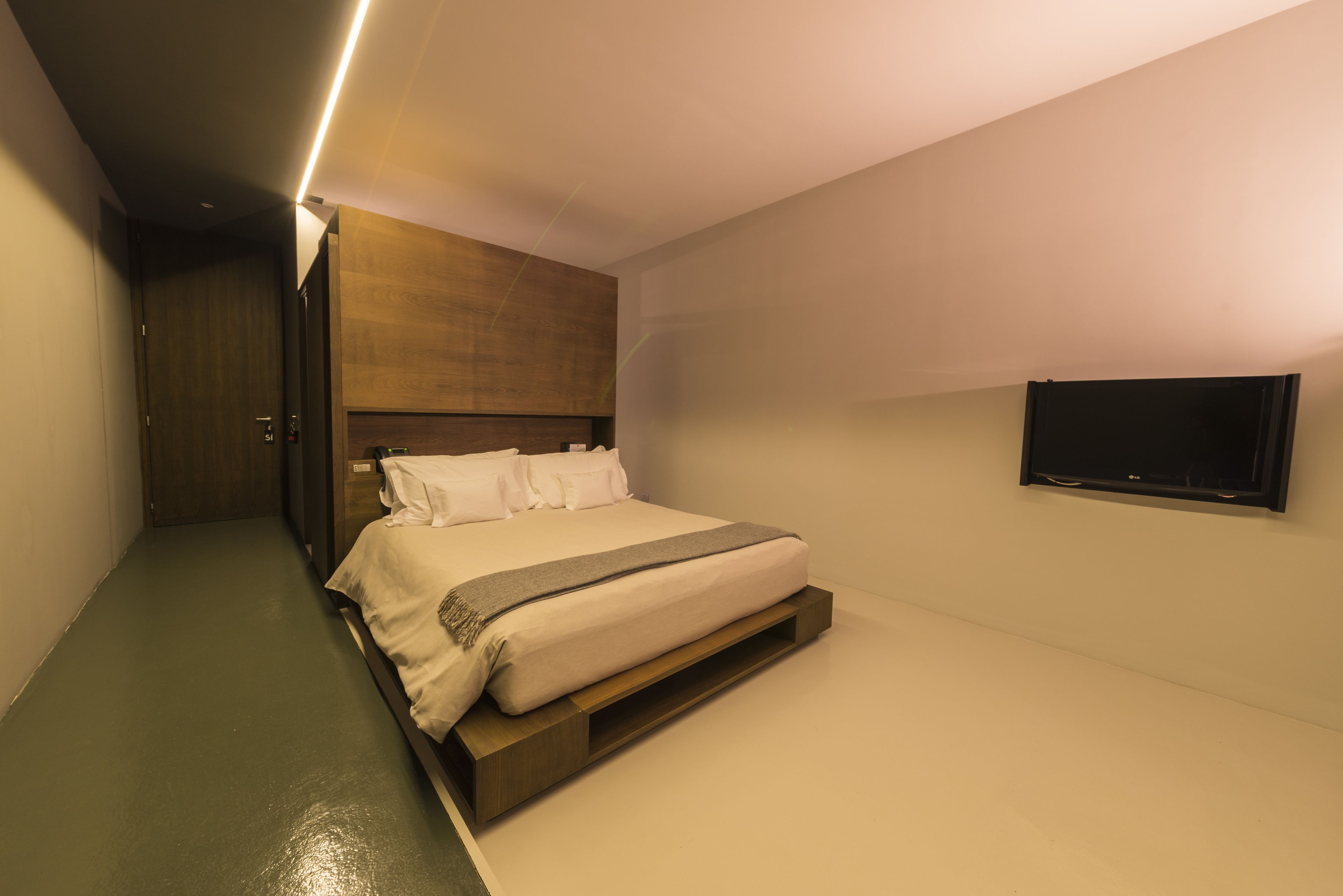 A modern hotel room with a large bed, a flat-screen TV mounted on the wall, and a wooden headboard.
