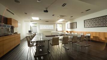 A conference room with a long table, chairs, a projector screen, and a kitchen area.