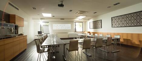 A conference room with a long table, chairs, a projector screen, and a kitchen area.