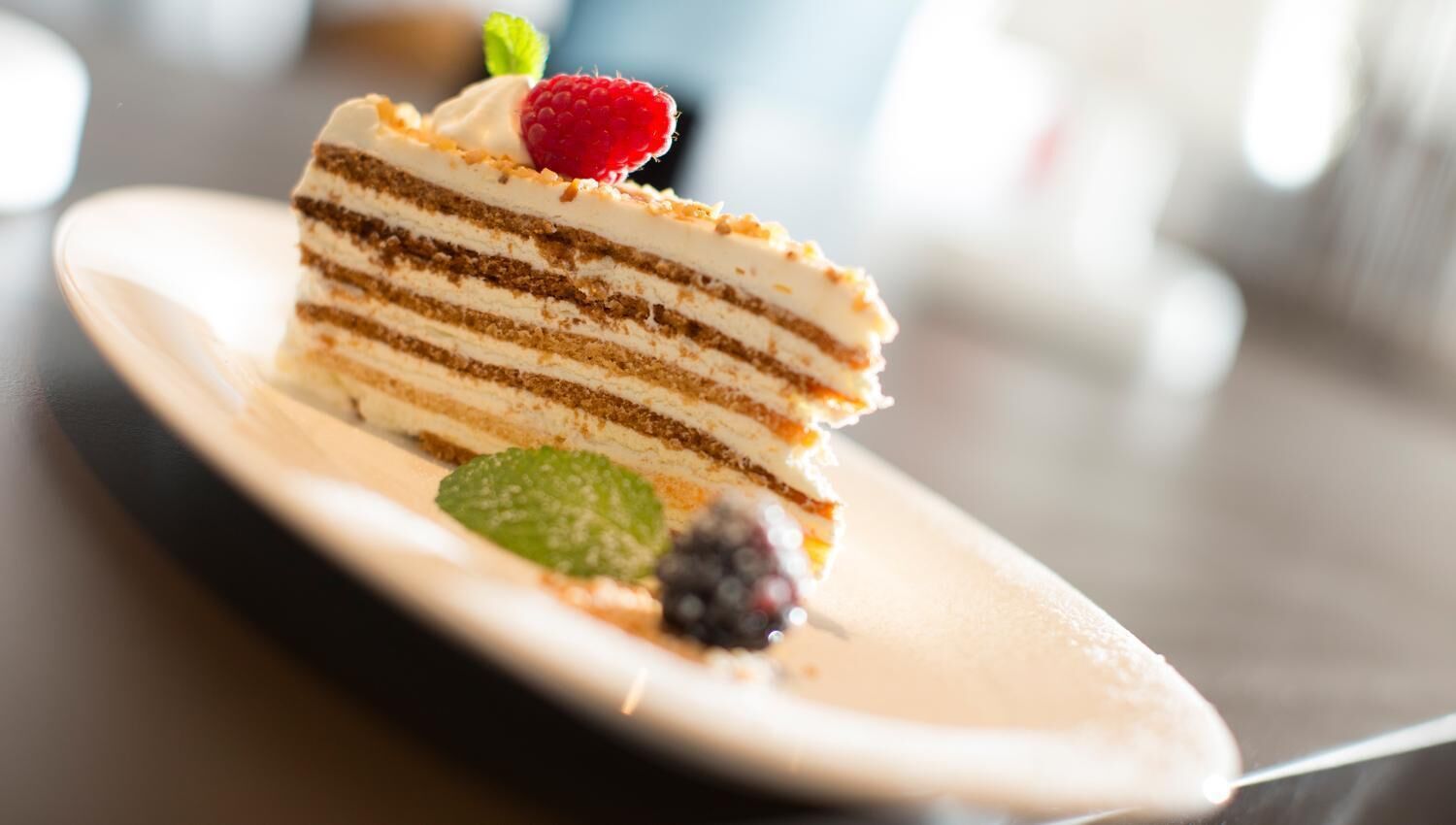 Une part de gâteau à plusieurs couches, garnie de crème et de fruits rouges, présentée sur une assiette.
