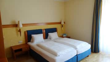 A hotel room with a double bed, two bedside tables, a nightstand, a lamp, and a window with curtains.