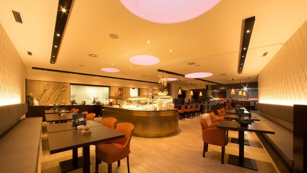 A modern restaurant with a central bar area, multiple seating options including booths and tables, and a warm, ambient lighting.