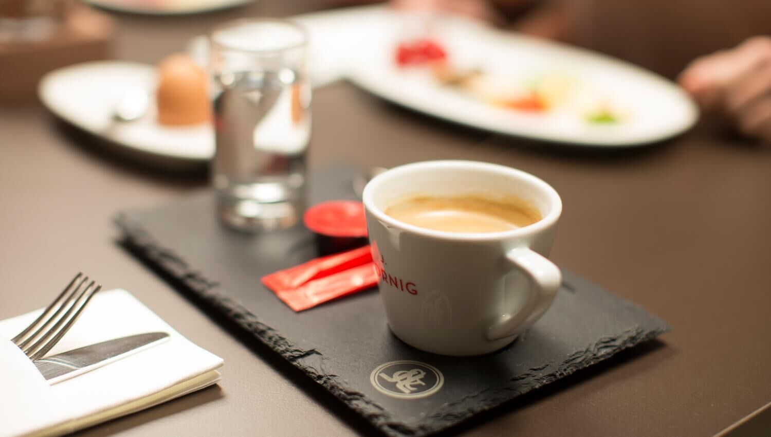 A table setting with a white cup of coffee, a glass of water, and a plate with food.