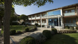 A hotel with a covered entrance, a check-in desk, and a well-maintained garden with hedges and a tree.