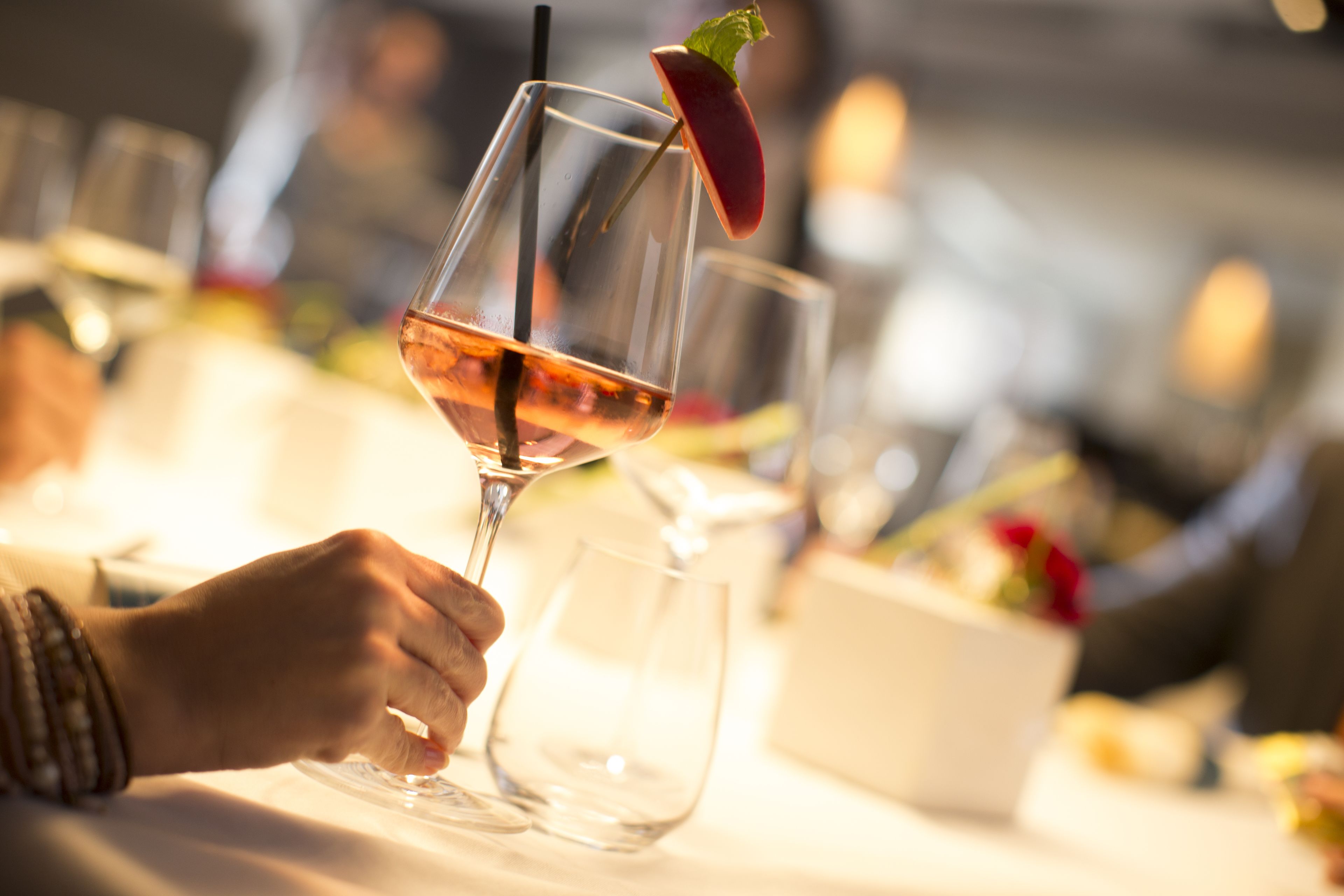 A close-up of a wine glass with a stem, a slice of fruit garnish, and a straw.