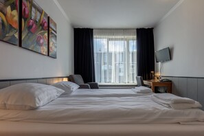 A hotel room with two beds, a large window with curtains, a flat-screen TV, and a painting on the wall.