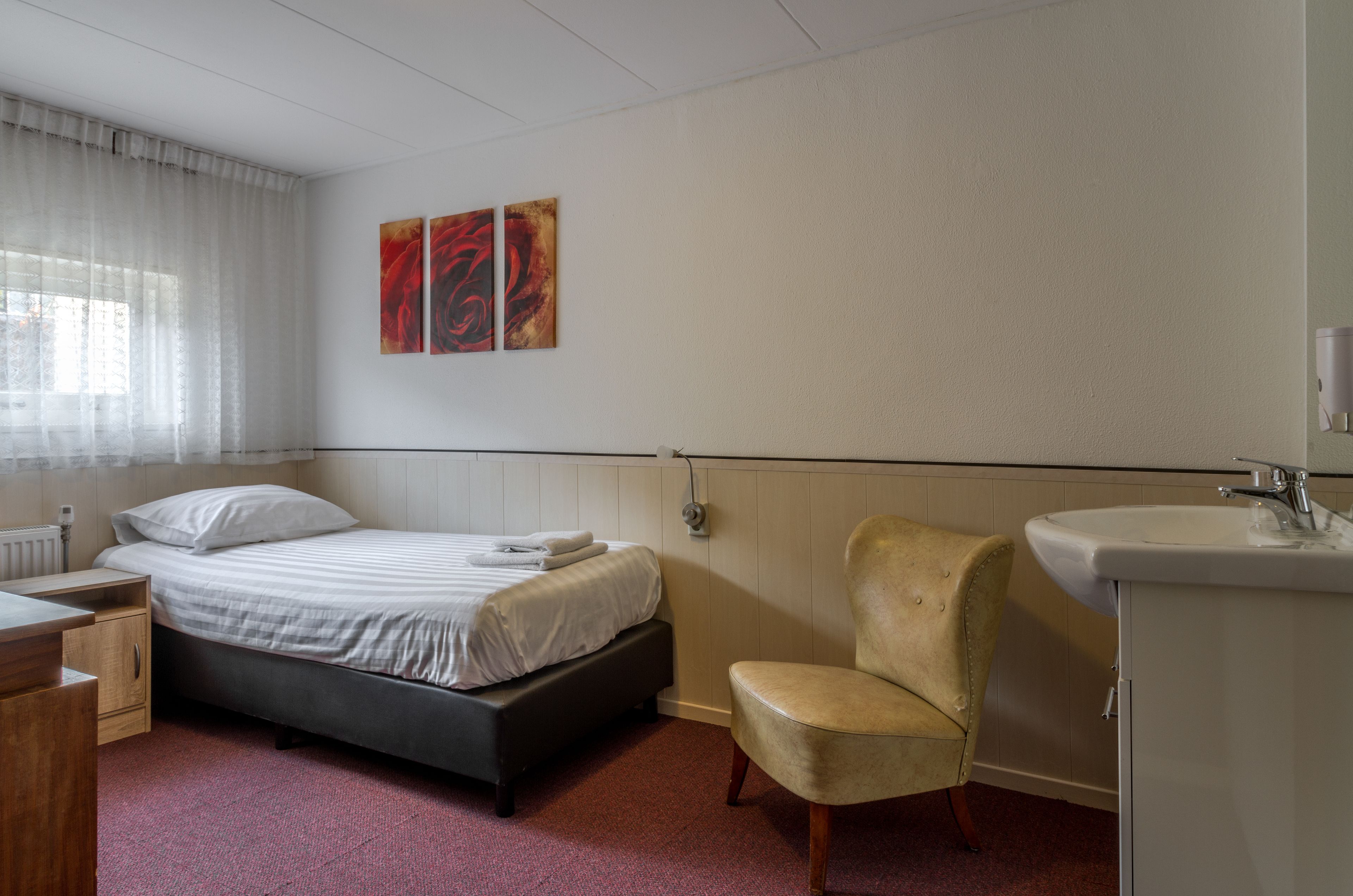 Ein Hotelzimmer mit Bett, Sessel, Nachttisch, Heizkörper und einem an der Wand hängenden Kunstwerk.