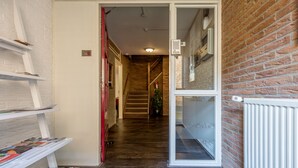 Een hal met een houten vloer, een blauwe mat bij de ingang, een bakstenen muur en een witte radiator.