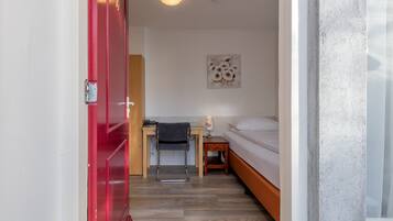 A room with a bed, a desk, a chair, and a red door.