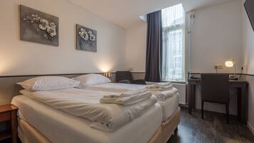 A hotel room with a large bed, a desk, and two wall-mounted paintings.