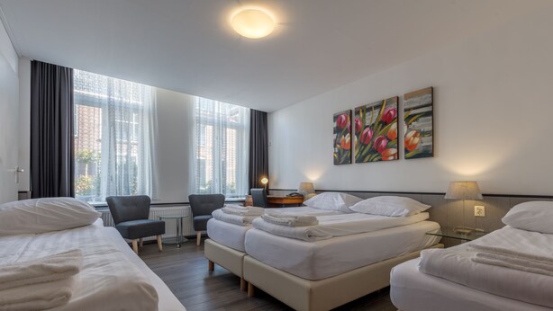 Een hotelkamer met twee bedden, een bureau en een stoel. Twee schilderijen hangen aan de muur en er is een raam met gordijnen.