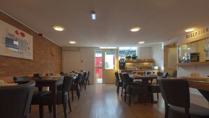 Een restaurant met houten vloeren, zwarte stoelen en gedekte tafels. Er is een receptiehoek met een bord boven de deur.