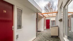 Een smalle gang met een rode deur met daarop '20', een beige berging en een glazen deur naar een kamer.