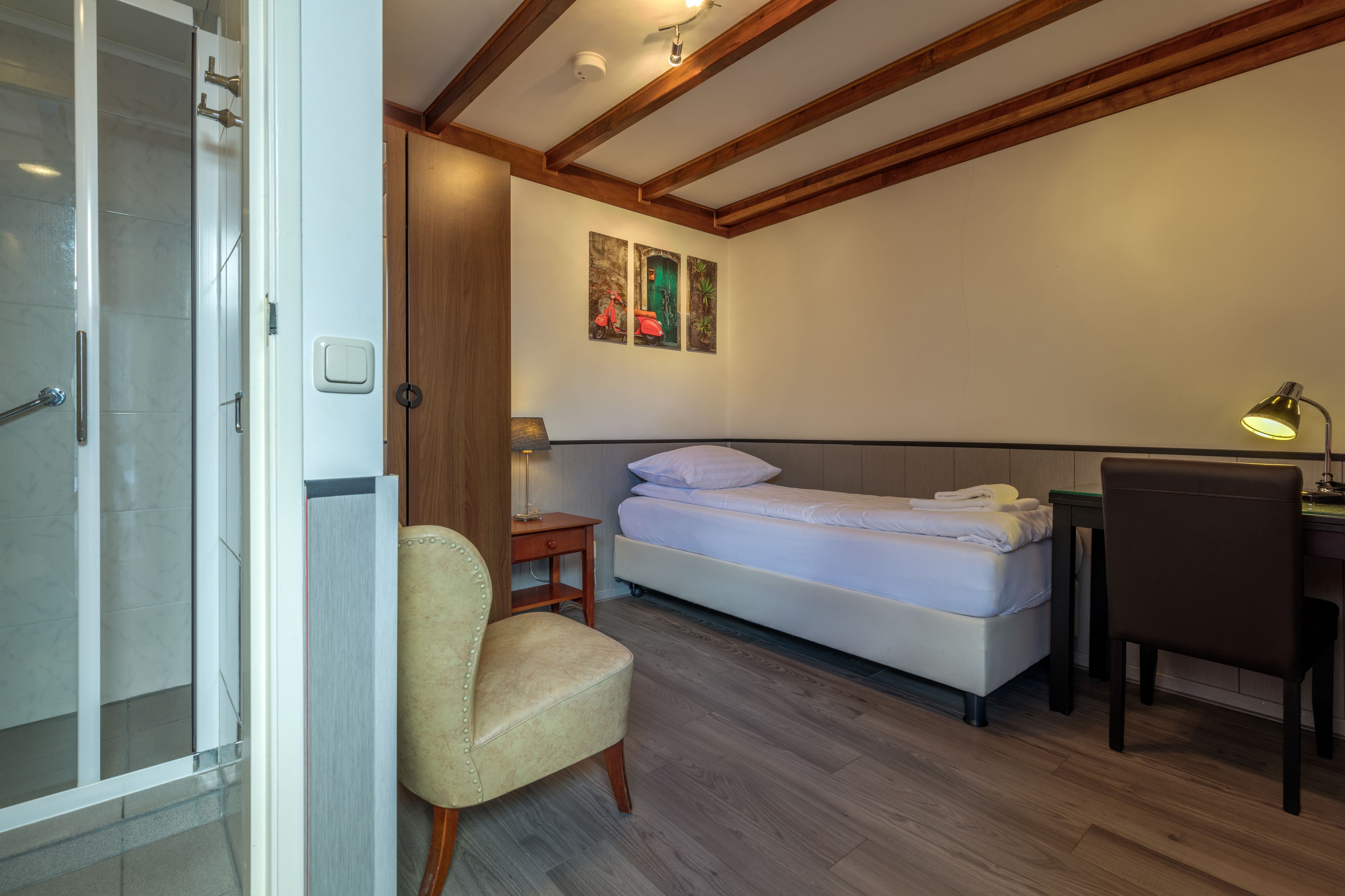 Un dormitorio con cama, escritorio, silla, lámpara y zona de ducha.