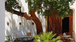 Una pared blanca con un gran tronco de árbol, un banco blanco con un cojín amarillo y una mesa de madera con sillas.