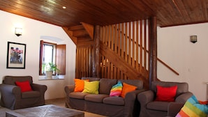 Una sala de estar acogedora con una escalera de madera, dos sofás con cojines de colores y una mesa de centro.