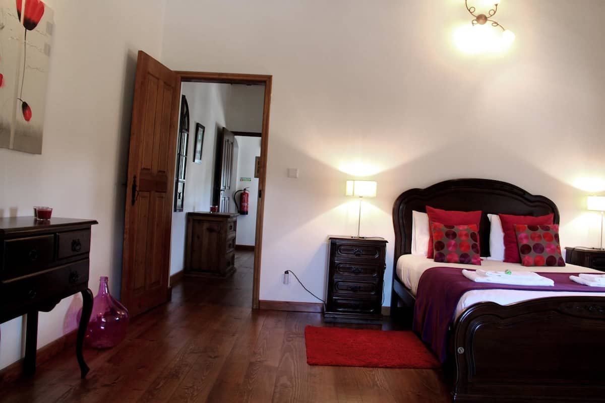 Un dormitorio con una cama de madera, almohadas rojas, una mesita de noche con lámpara, un aparador y una alfombra roja.