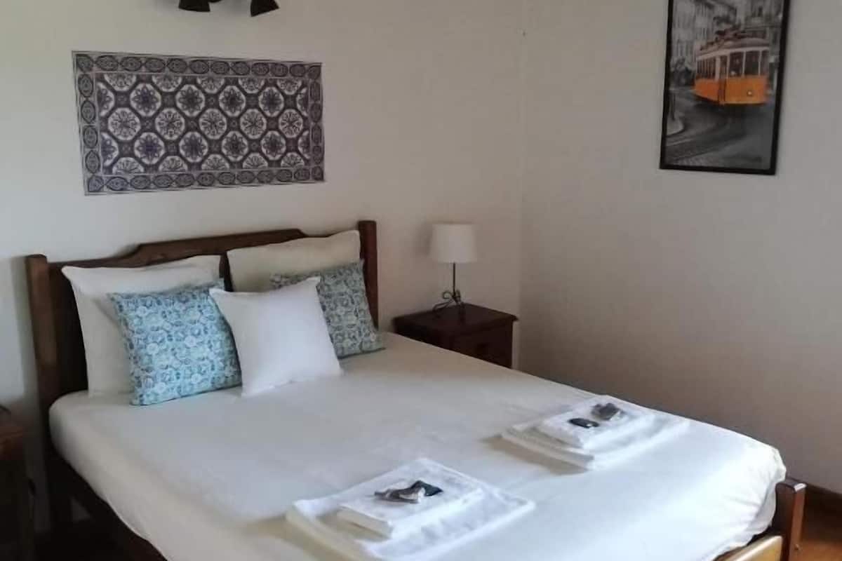 Una cama bien hecha con sábanas blancas, un tapiz decorativo en la pared y un cuadro con la imagen de un tranvía.