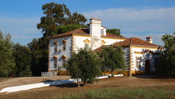 Un edificio grande e histórico, con fachada simétrica, múltiples ventanas y una chimenea central.