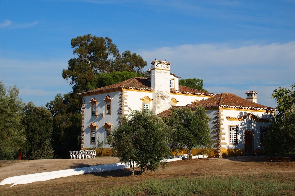 Un edificio grande e histórico, con fachada simétrica, múltiples ventanas y una chimenea central.
