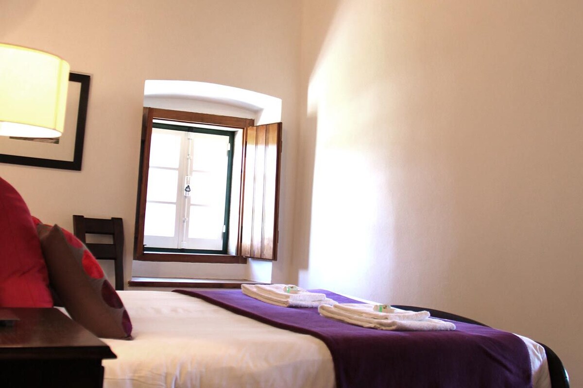 Un dormitorio con cama, ventana, lámpara y alfombra roja.