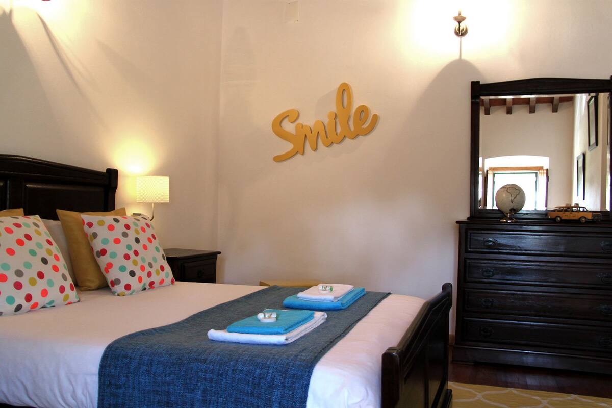 Una cama bien hecha con almohadones de lunares, una colcha azul y un cartel en la pared que dice 