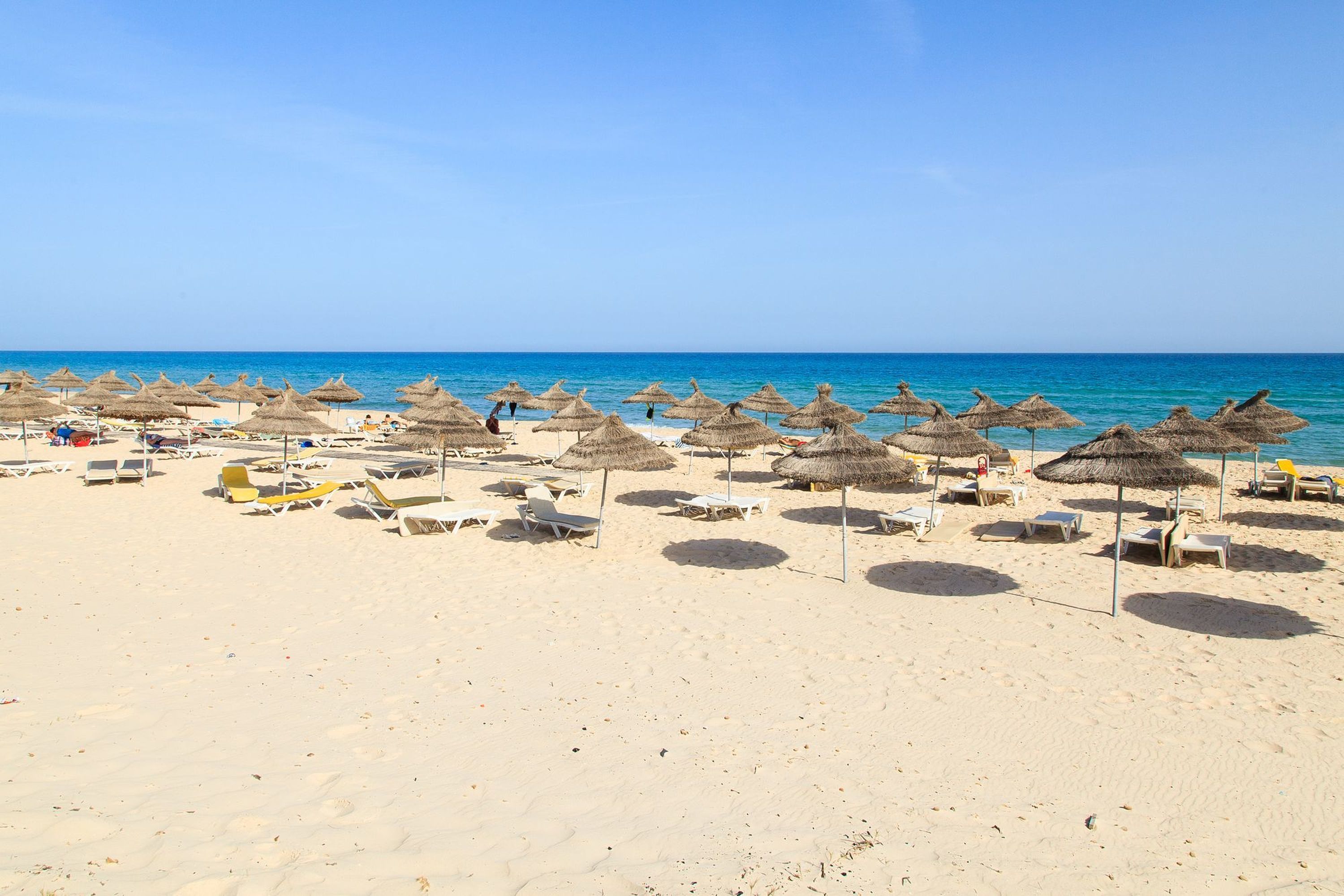 Une plage bordée de rangées de chaises longues et d’ombrelles en chaume.