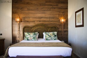 Un lit avec une tête de lit en bois, deux lampes fixées au mur et un tableau encadré accroché au mur.