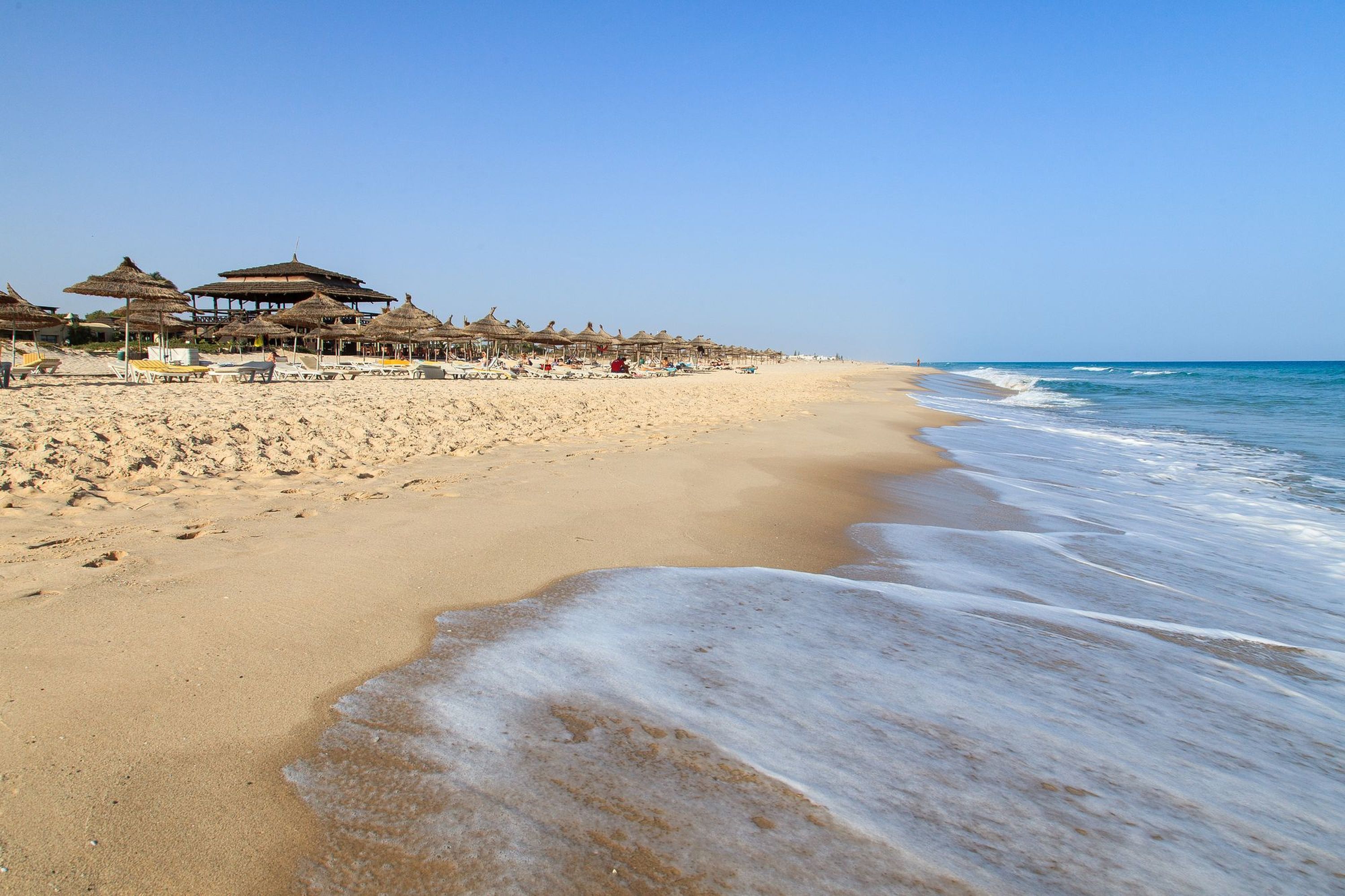 A beach with thatched-roof structures and sun loungers along the shore.