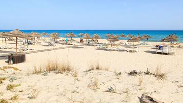 A beach with sun loungers and thatched umbrellas.