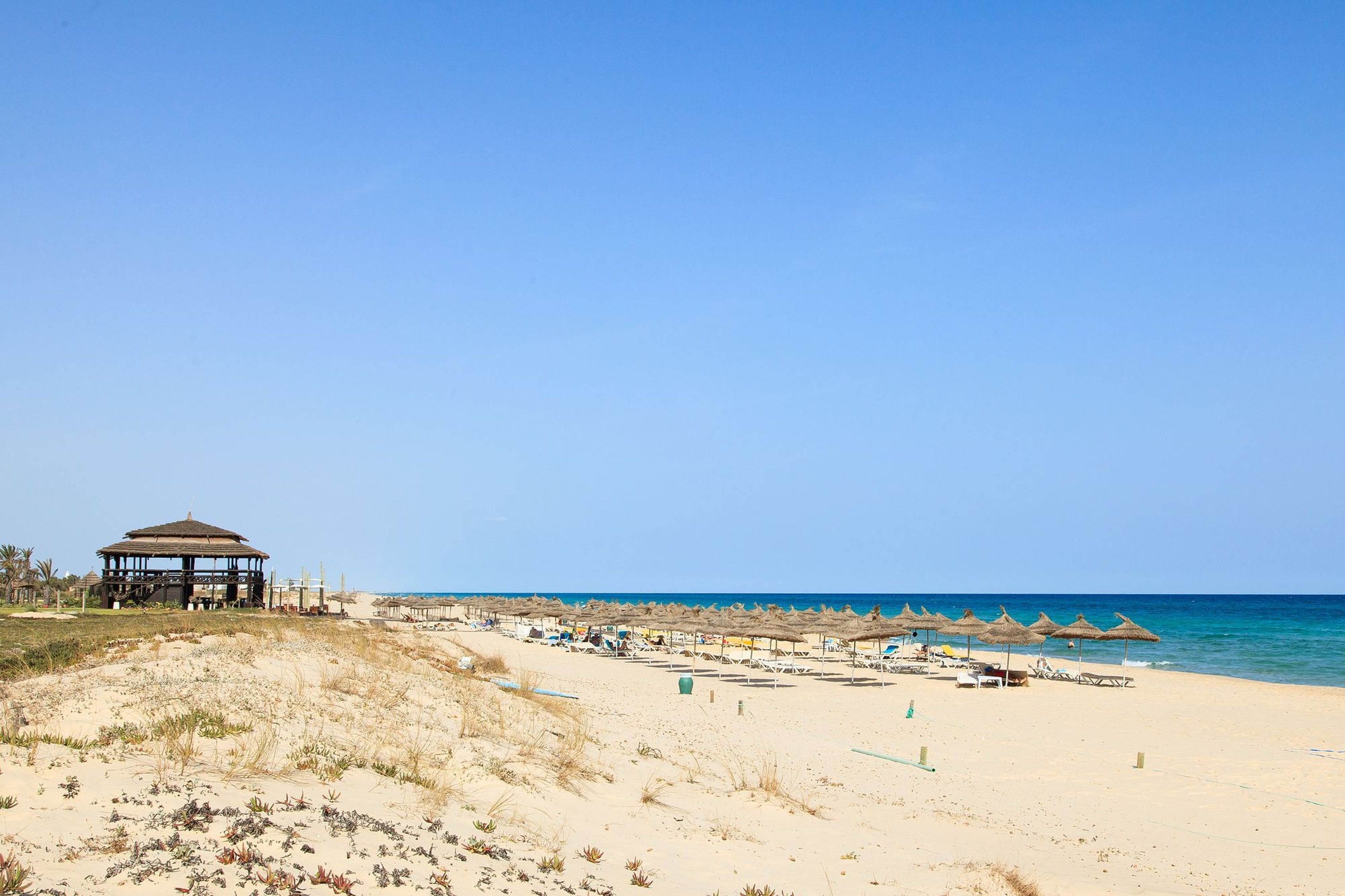 A beach with a gazebo, beach umbrellas, and lounge chairs.