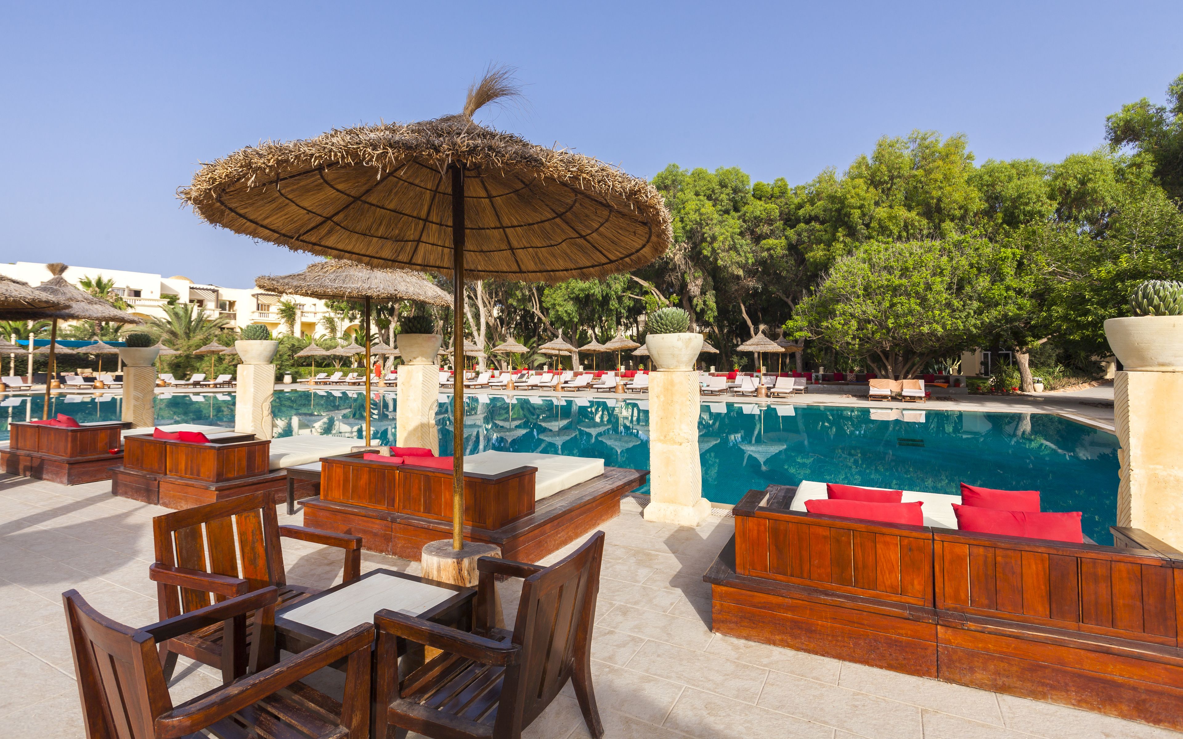 A poolside area with wooden furniture, thatched umbrellas, and lounge chairs.