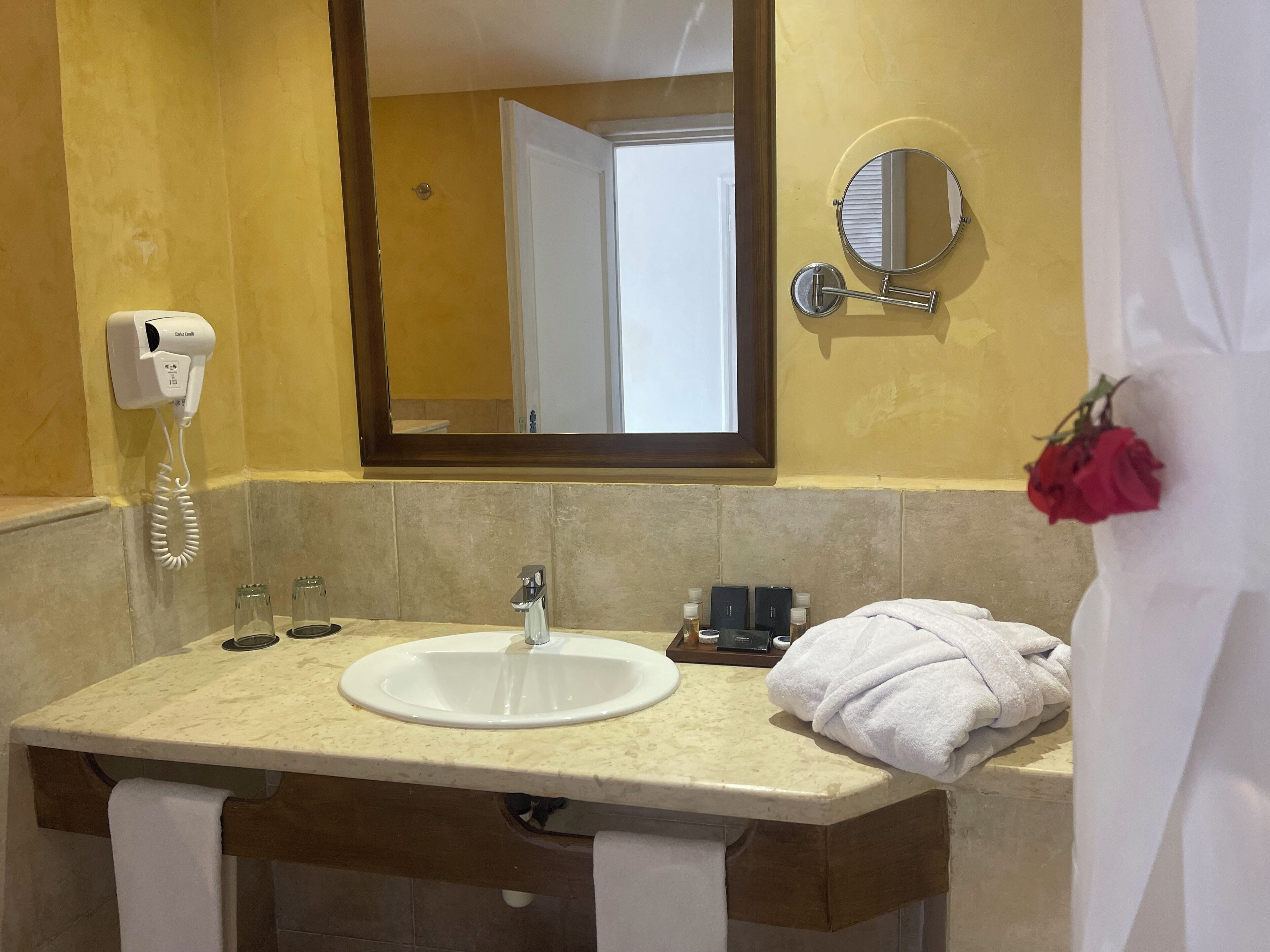 Un baño con lavamanos, espejo y secador de pelo en la pared.