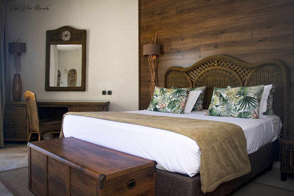 A bedroom with a large bed, a wooden headboard, a bedside table, a mirror, and a lamp.