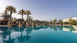 Une piscine d’un bleu éclatant, bordée de palmiers et dotée d’espaces de repos à l’ombre.