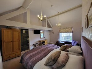 A bedroom with a large bed, wooden wardrobe, and a desk with a chair.
