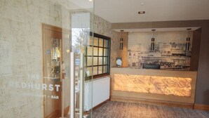A reception area with a wooden reception desk, a glass partition, and a wall with a cityscape mural. - The Redhurst Hotel (Glasgow)