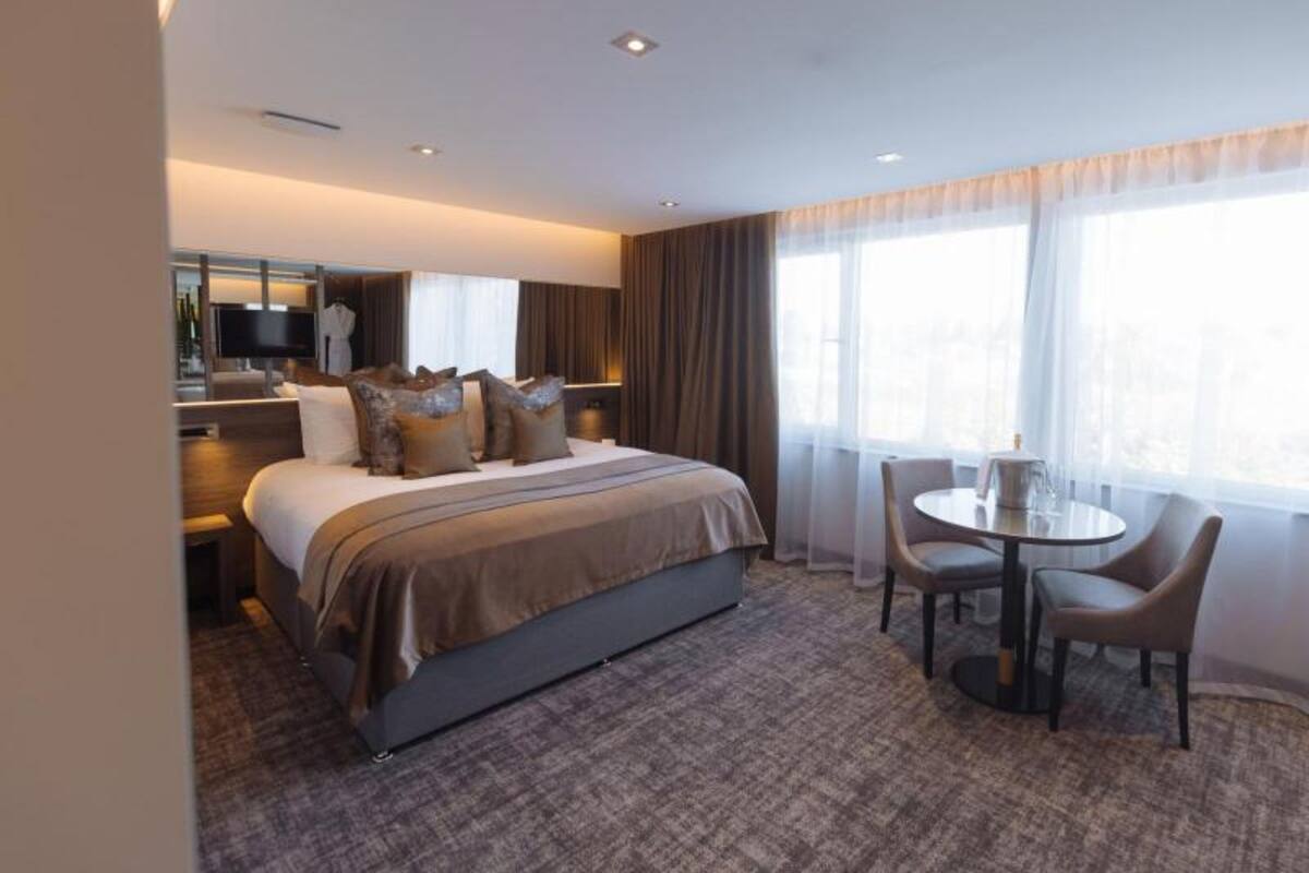 A hotel room with a large bed, a desk, a chair, and a window with curtains.