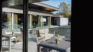 An outdoor seating area with tables and chairs, a glass wall, and a building with a sign in the background. - The Redhurst Hotel (Glasgow)